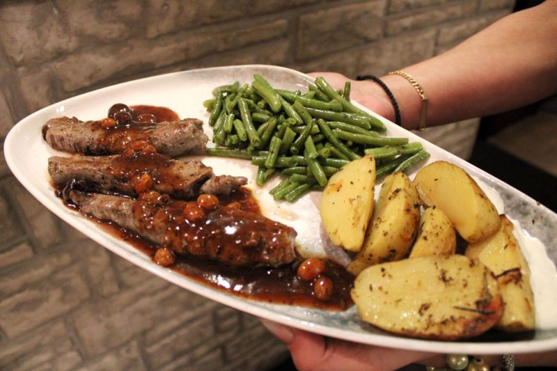 Ein Teller mit gegrillten Lammfilets in dunkler Soße mit grünen Bohnen und Kartoffeln