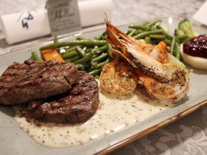 Rinderfilet und Scampi auf einem Teller angerichtet mit grünen Bohnen und Soße